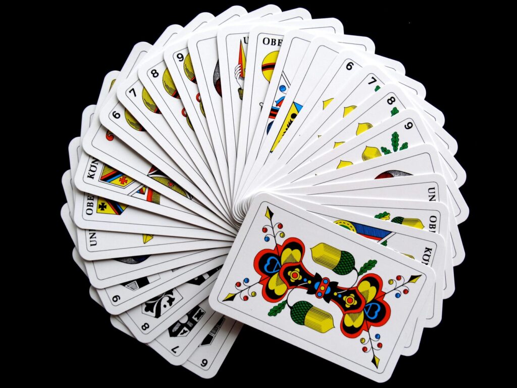 Prin ce diferă principalele variante de poker Cărți de joc așezate în evantai pe o masă de lemn, alături de câteva jetoane